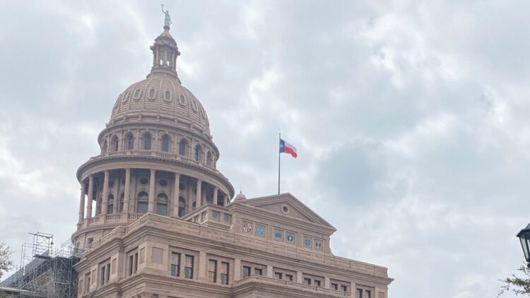 Top of the Texas State Capitol building with a Texas flag flying in the foreground.
