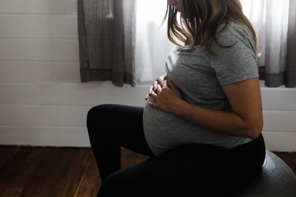 Full term pregnant person sitting on an exercise ball with her hands on her stomach