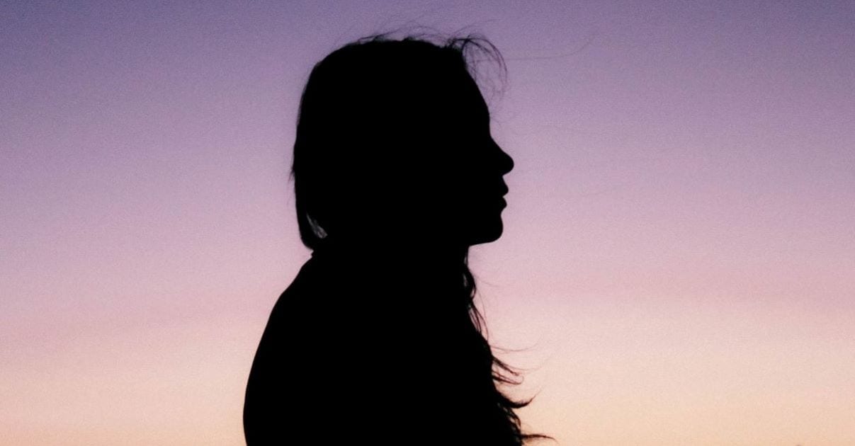 Silhouette of woman with long hair with sunset in background