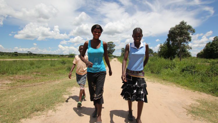 Young African women in Zambia walking on a dirt path