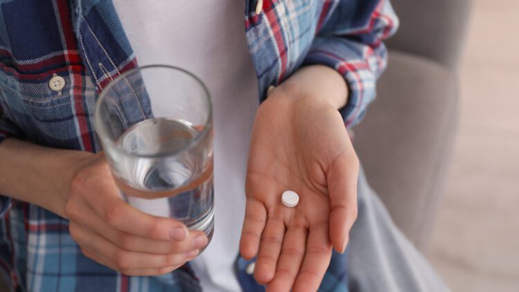 medication abortion - pills- Young woman with abortion pill and glass of water indoors, closeup