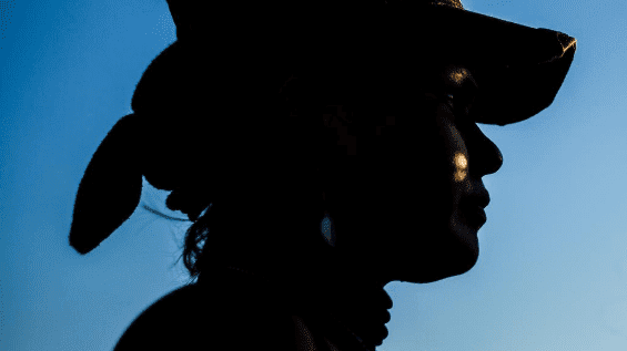 Close up of woman wearing a baseball cap and bandana, silhouetted against the sky
