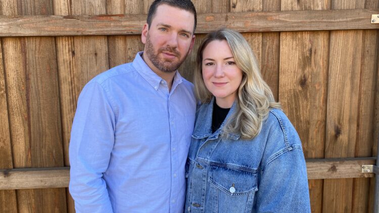 Headshot of Justin and Kate Cox standing in front of a wooden fence.