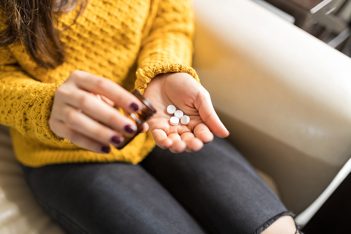 women with pill bottle, pouring pills in her hand