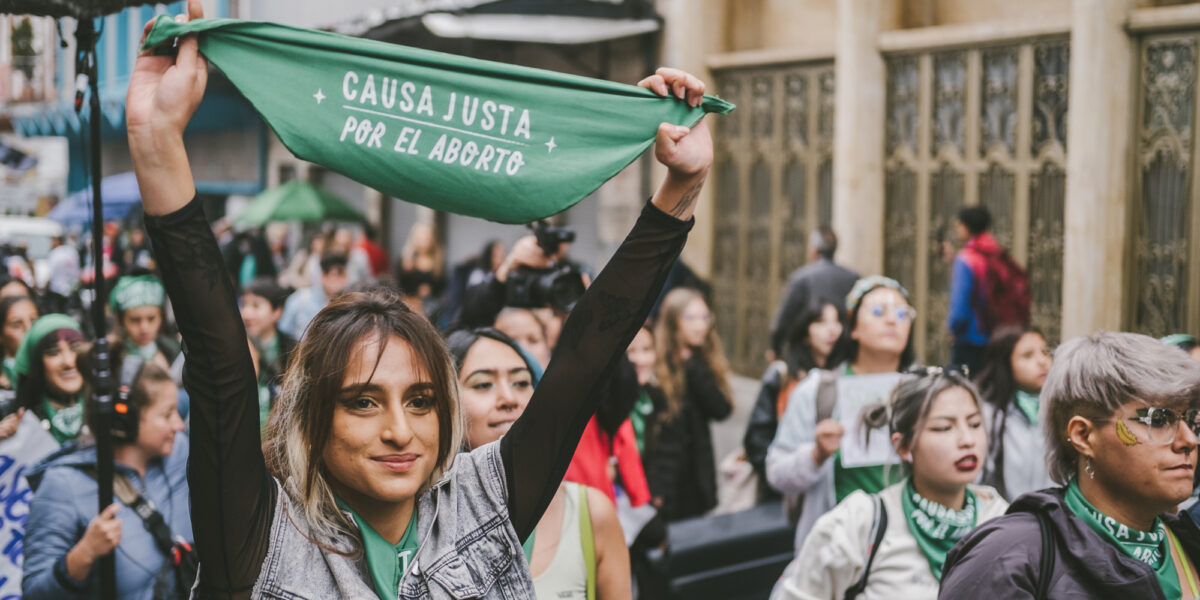 Woman holding up Causa Justa flag in a crowd of protesters.