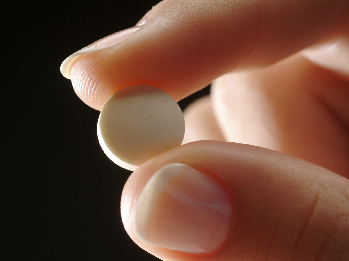 Two fingers holding an abortion pill.