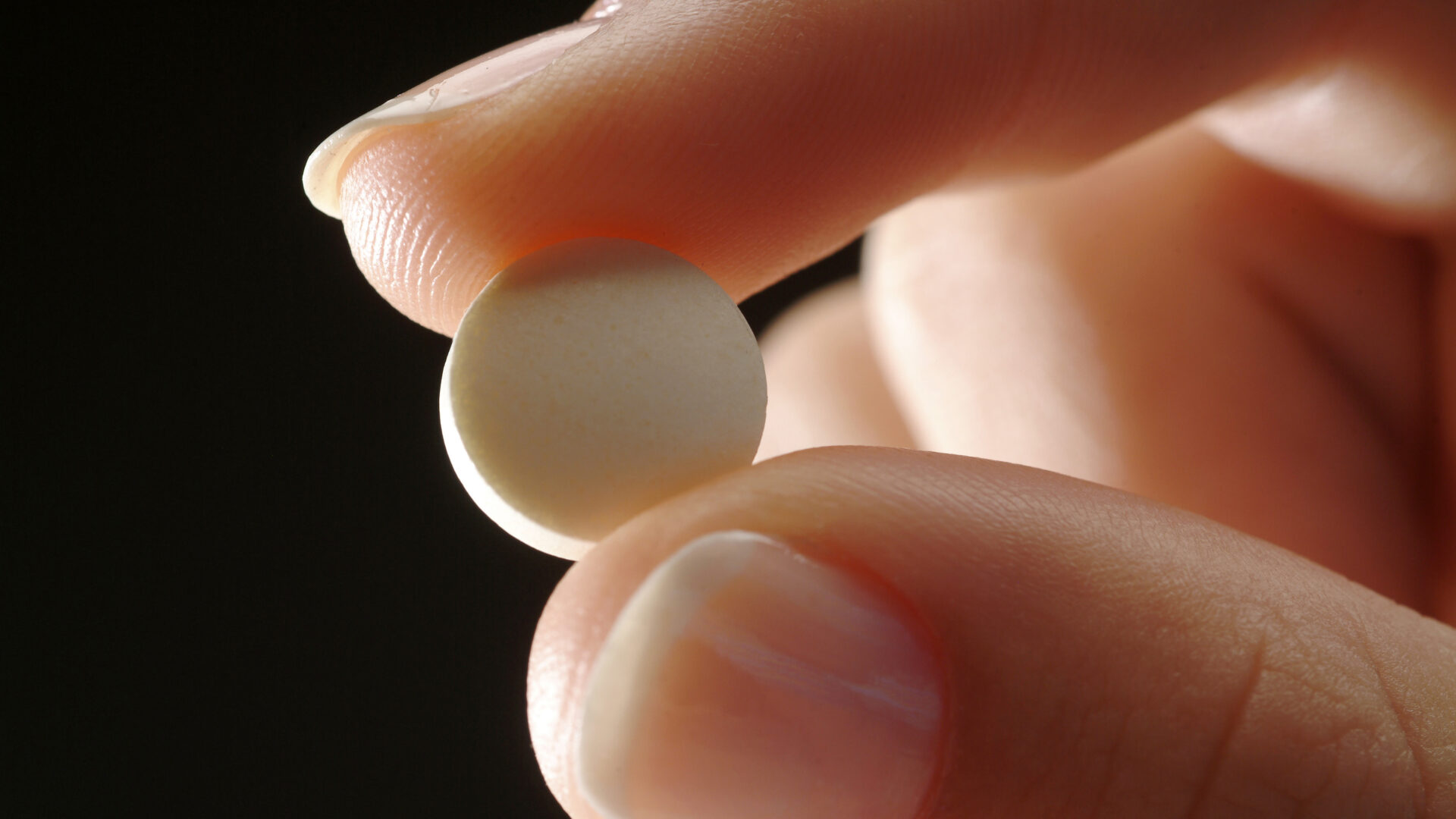 Two fingers holding an abortion pill.